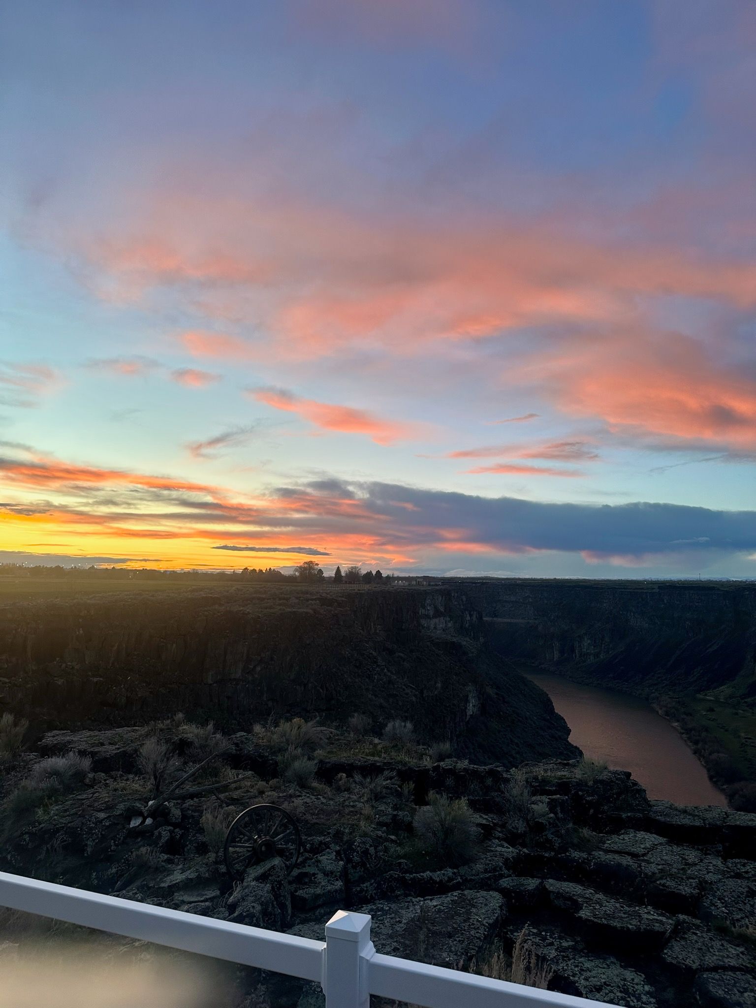 A sunset over a canyon with a white fence in the foreground.