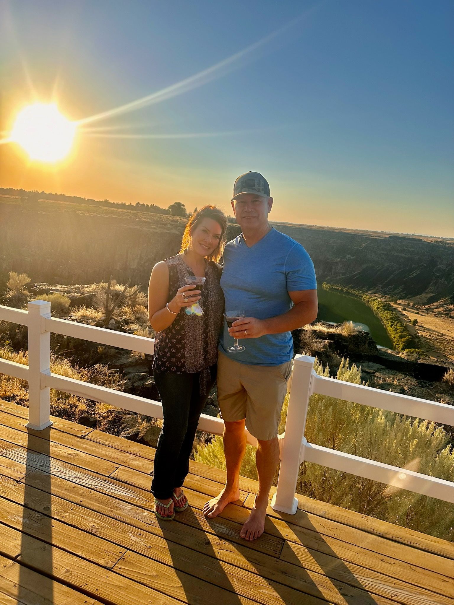 Couple on deck with wine glasses at sunset, overlooking canyon.