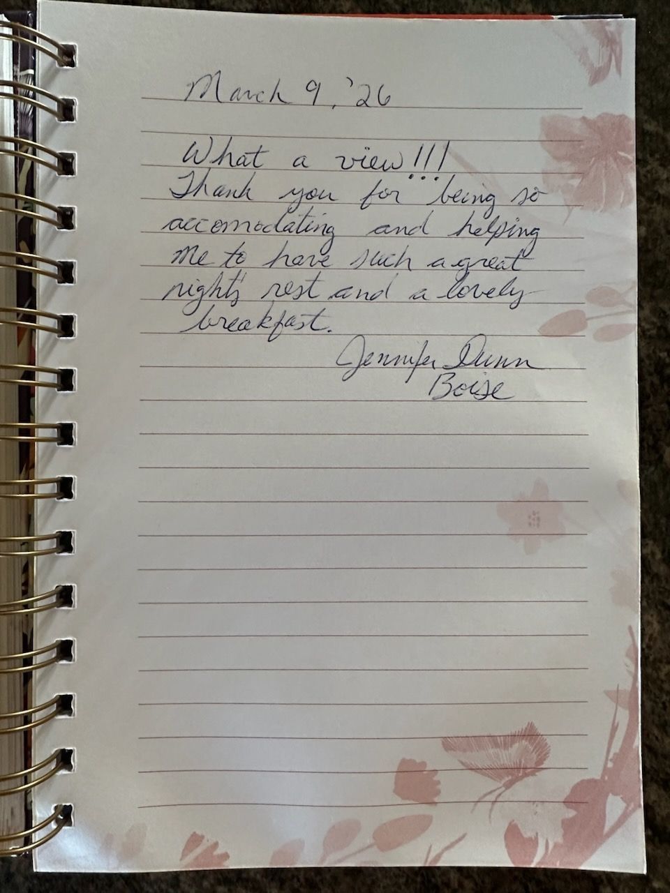 Handwritten note on a lined spiral notebook page with pink floral corners and red stamp marks.