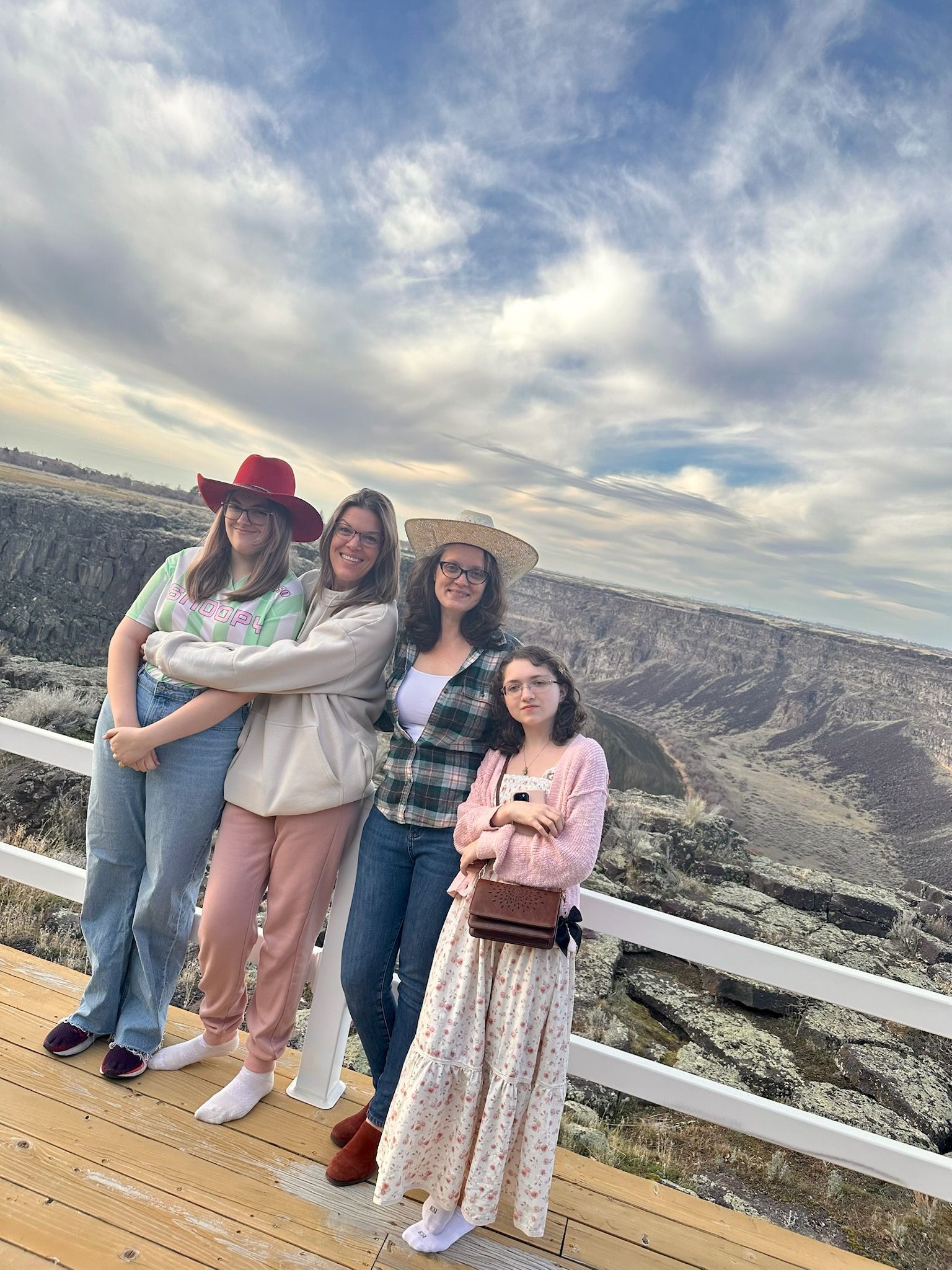 Four friends posing by a scenic canyon overlook with white railings under a cloudy sky