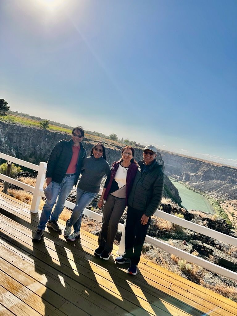 Four people posing on a wooden deck with a canyon and river in the background on a sunny day