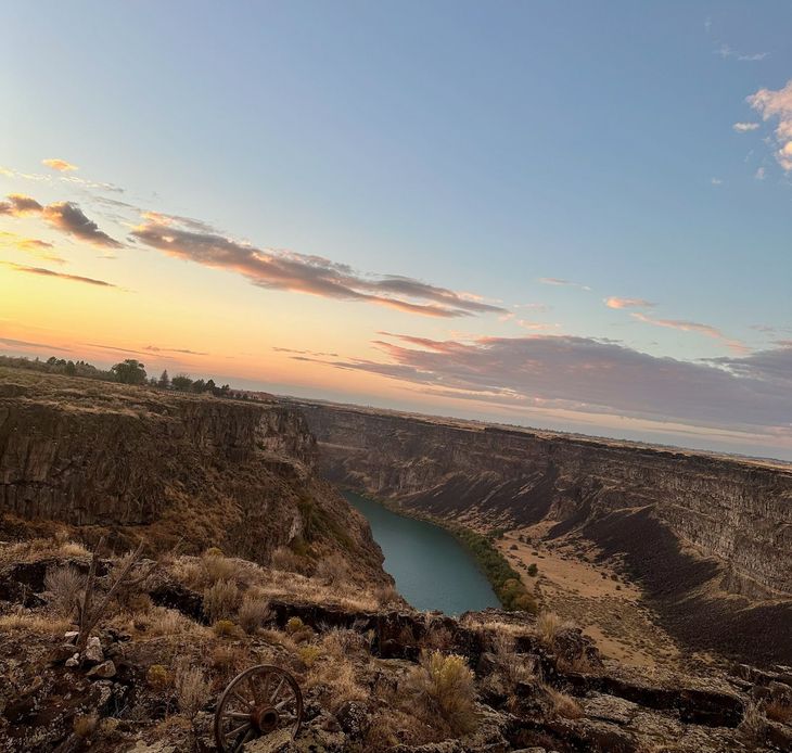 Sunset over a rocky canyon with a winding blue river below and a pastel sky