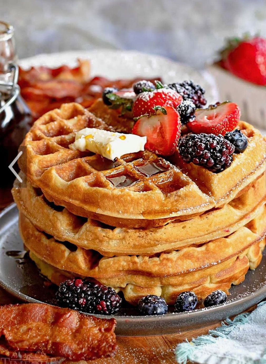 Stack of golden waffles topped with butter, strawberries, and blackberries on a plate.