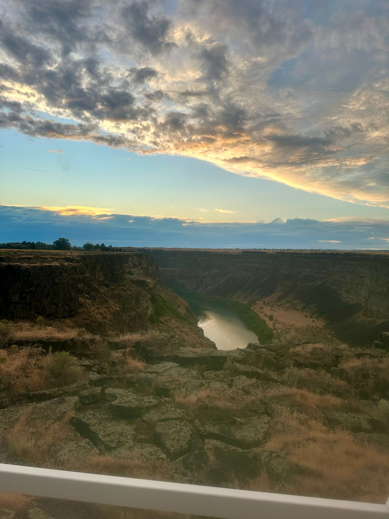 Sunset over a rocky ravine with a narrow river and dramatic clouds in a blue sky