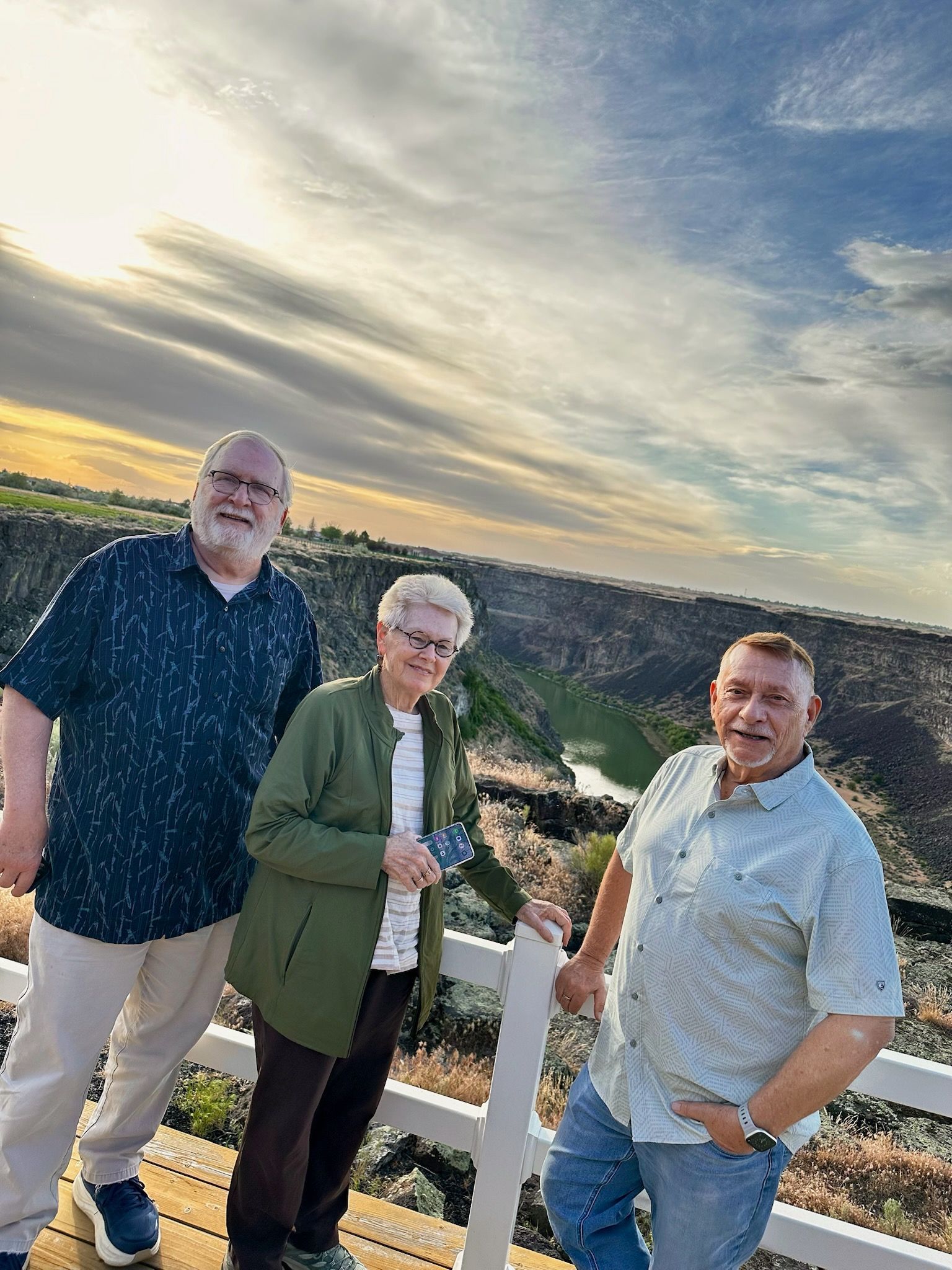 Three people standing by a hillside overlook at sunset with a cityscape below.