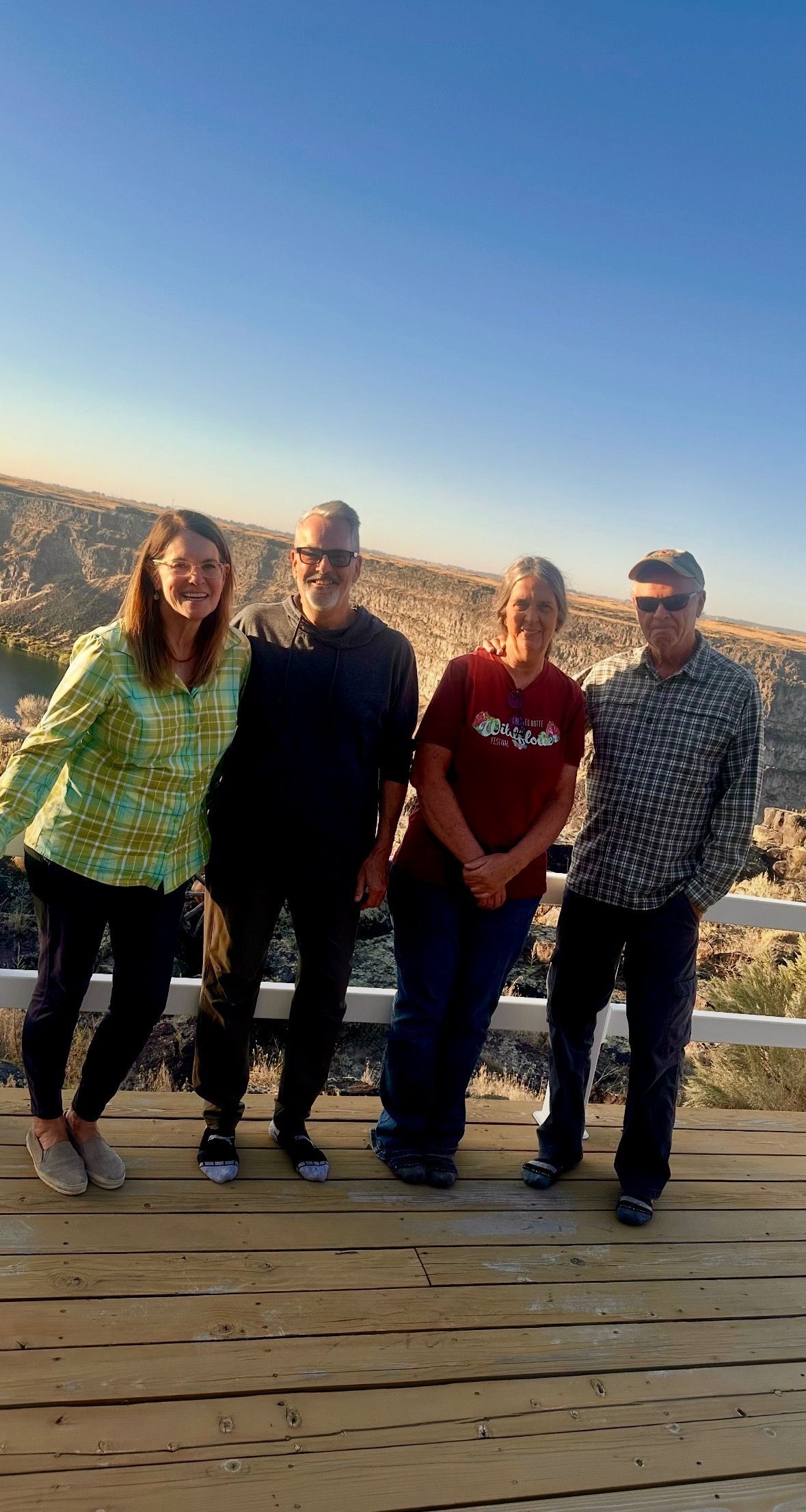 Four people smiling, posing on a wooden deck with a canyon and blue sky in the background.
