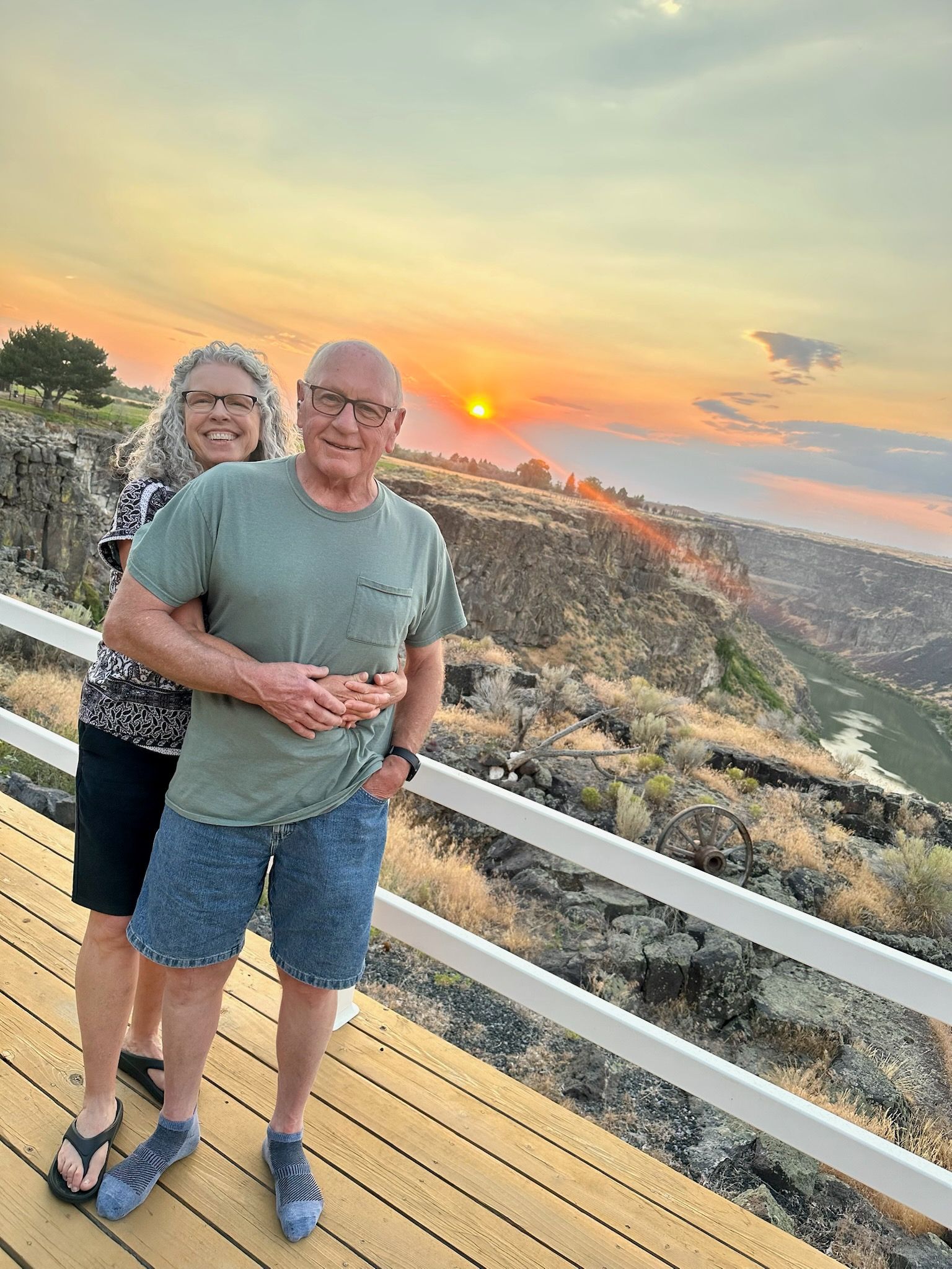 Couple hugging on a wooden deck, overlooking a canyon at sunset.