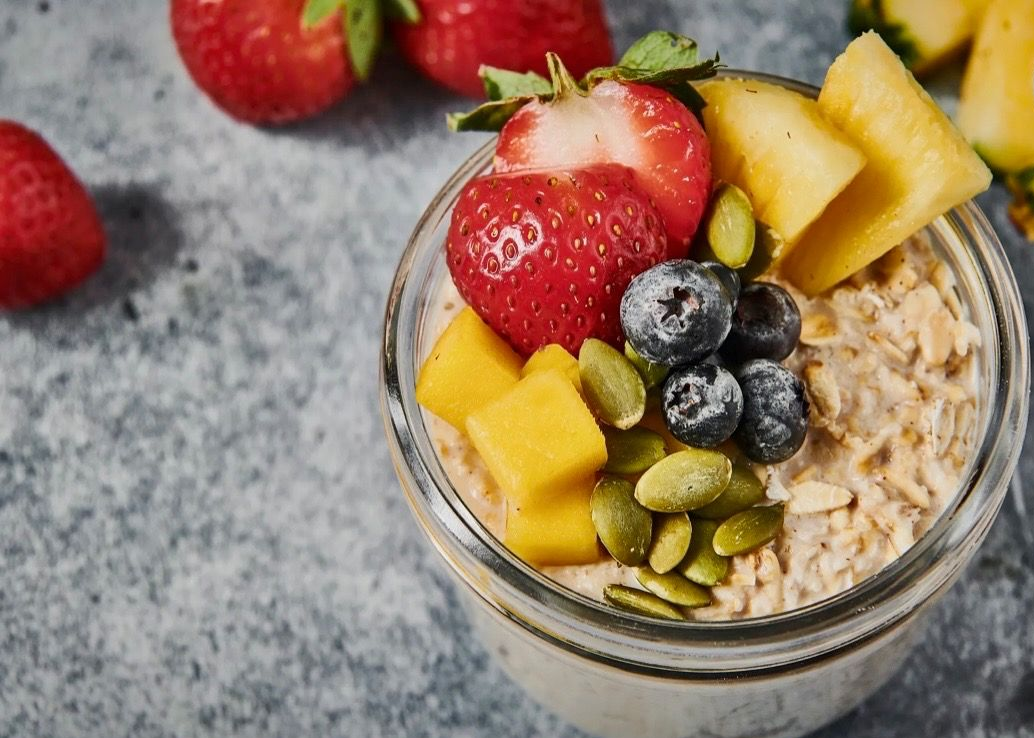 Overhead view of oatmeal topped with strawberries, blueberries, mango, and pumpkin seeds in a glass jar