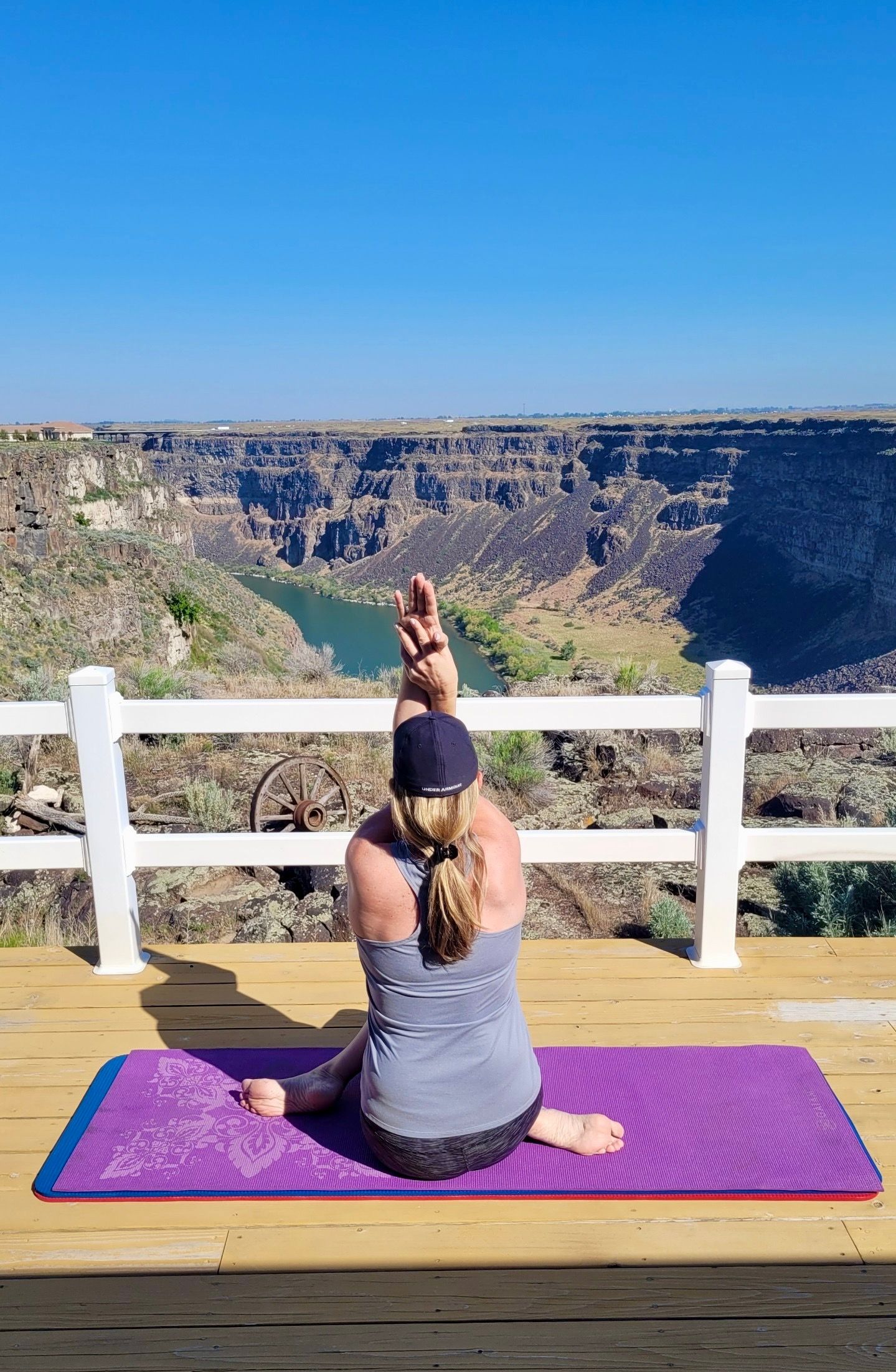 Woman in yoga pose on a mat, arms intertwined, overlooking canyon and river.