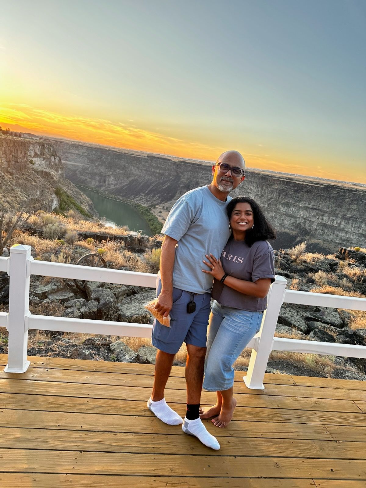 Couple standing on a wooden deck at sunset with a white fence and canyon view behind them
