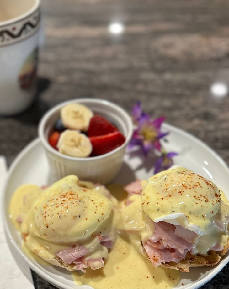 Eggs Benedict with hollandaise, ham, fruit cup, and coffee on a restaurant table