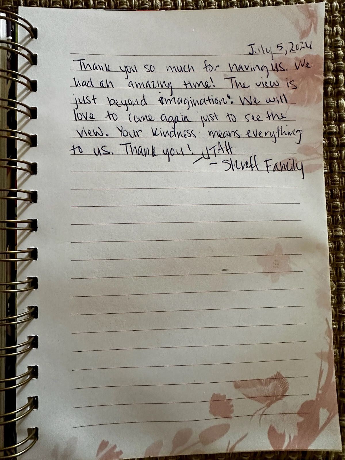 Handwritten note on lined spiral notebook paper with floral border on a wooden surface