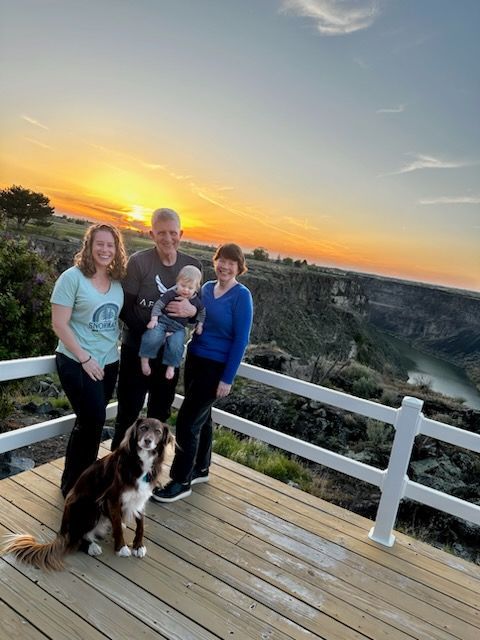 Four people and a dog on a wooden overlook at sunset, with a canyon and glowing sky behind them.