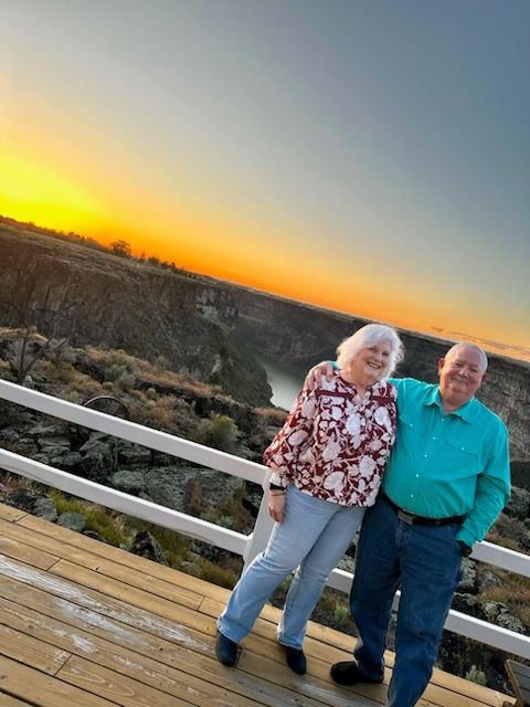 Two people standing on a wooden deck at sunset, with a scenic valley in the background.