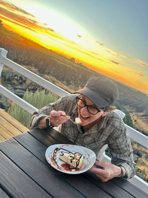 Woman laughing, eating dessert on a deck at sunset.