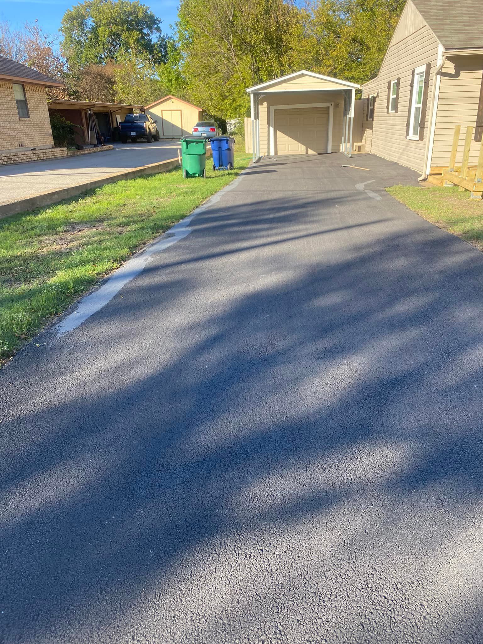 A driveway leading to a house with a garage and trash cans.
