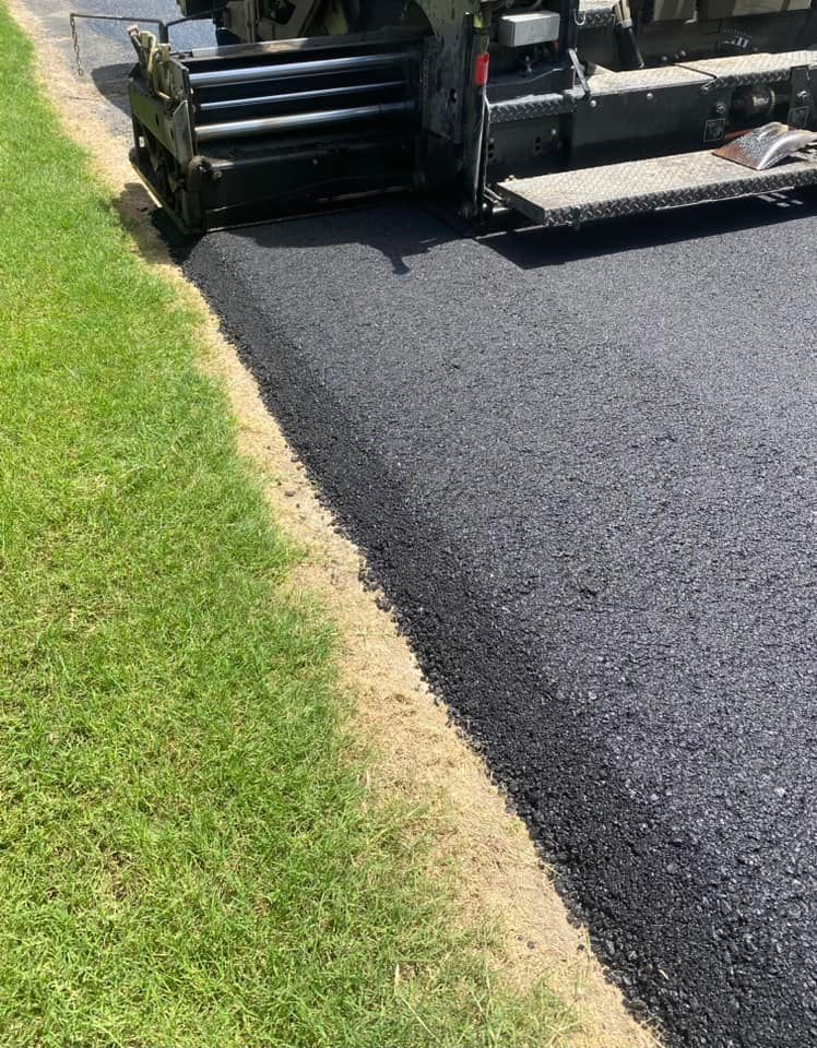 A machine is laying asphalt on the side of a road.