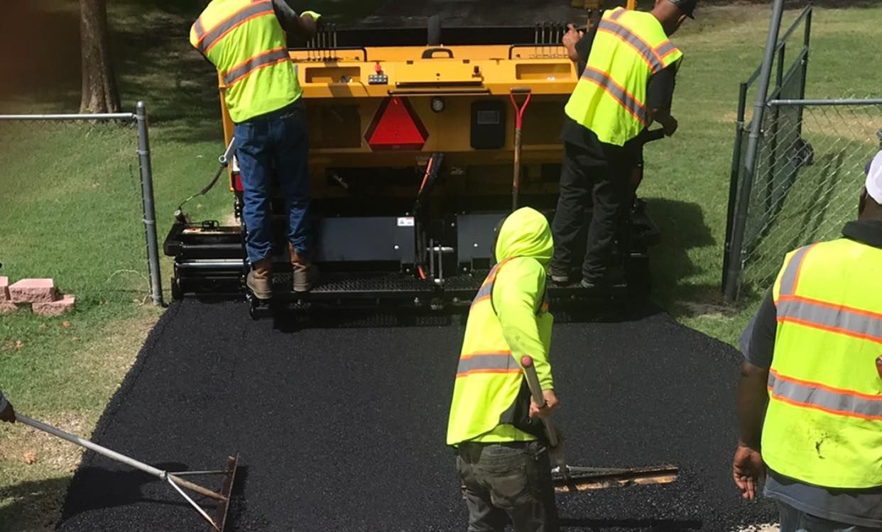 A man is using a broom to spread asphalt on a road.