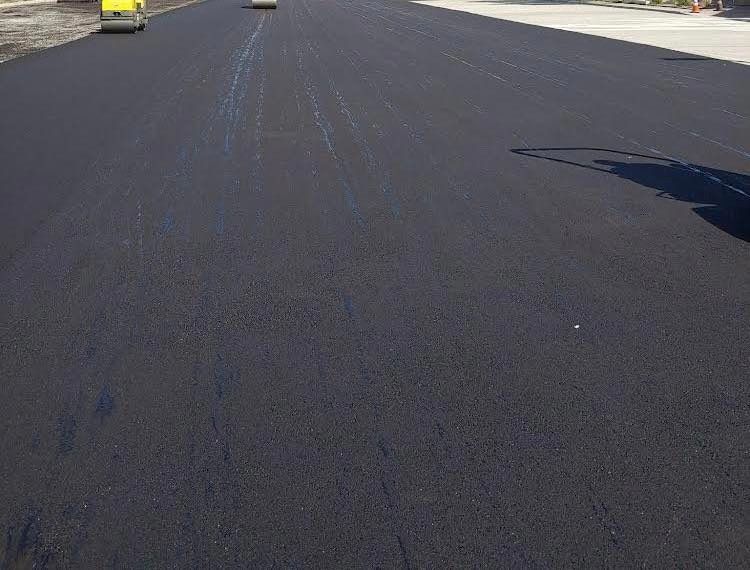 A black asphalt road with a yellow truck driving down it.
