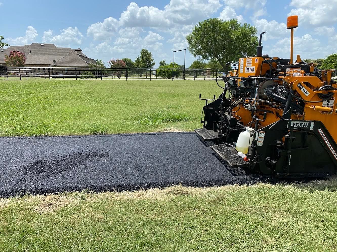 A machine is paving a road in a grassy field.