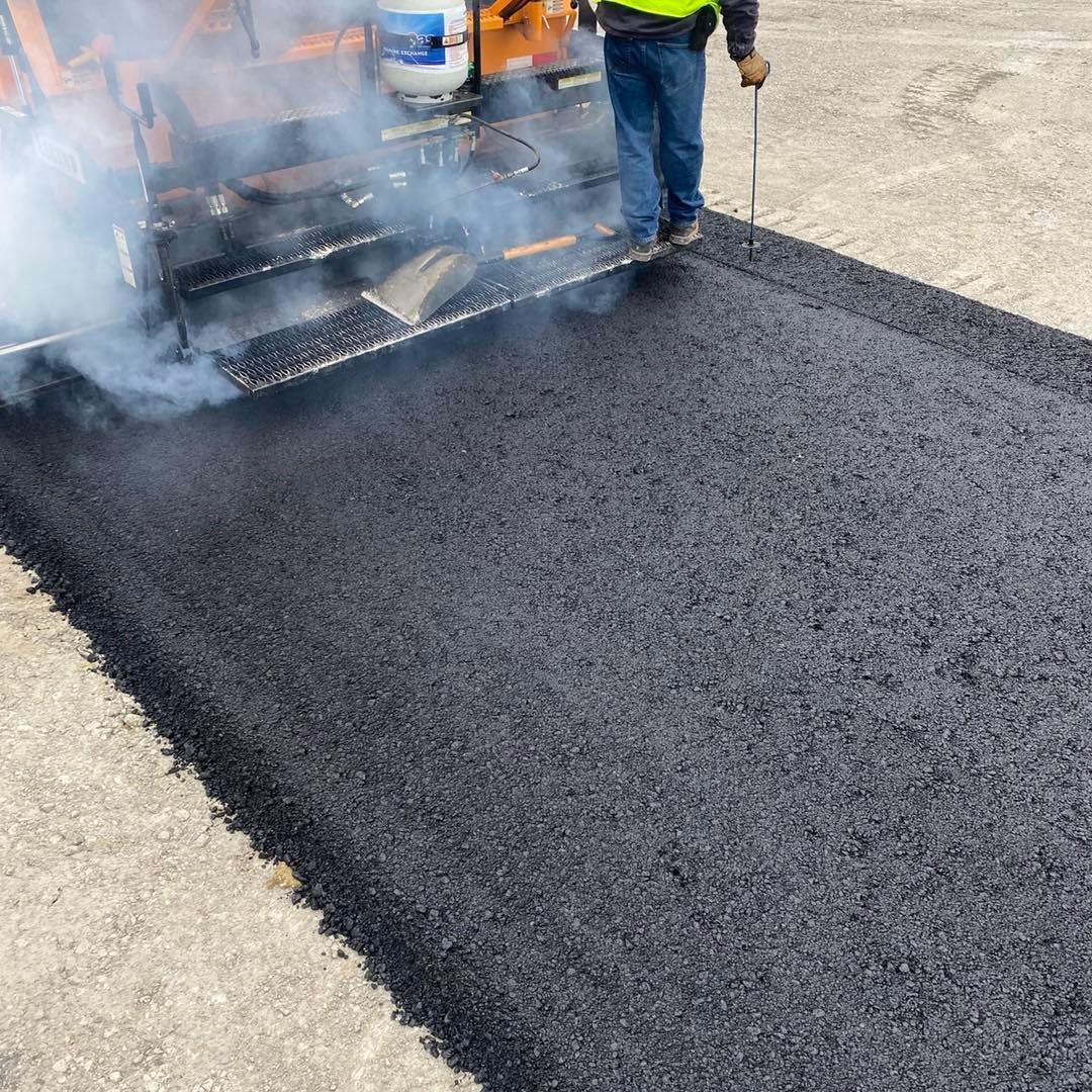 A man is spreading asphalt on a road with a machine.