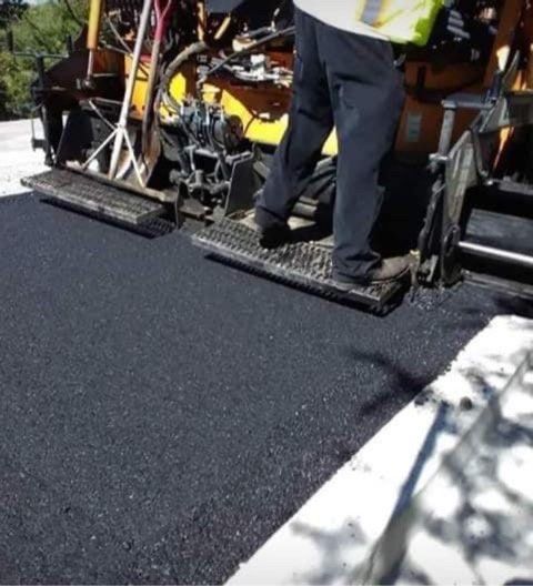 A man is standing next to a machine that is spreading asphalt
