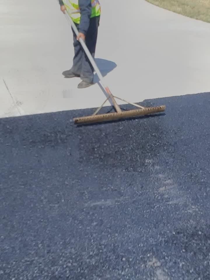 A man is using a broom to spread asphalt on a driveway.
