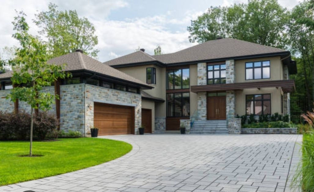 Two-story house with stone and tan facade, wooden garage door, and gray paver driveway.