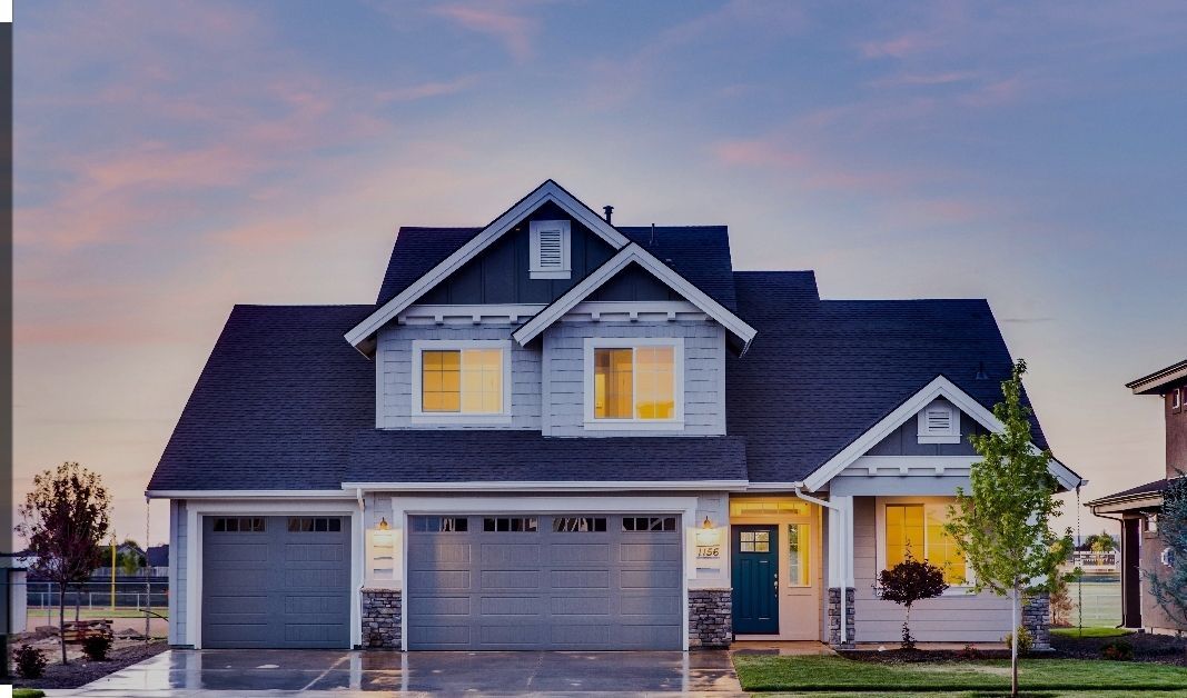 Two-story house with gray siding, blue door, and three-car garage; illuminated at dusk.