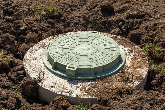 A green manhole cover is sitting in the middle of a dirt field.