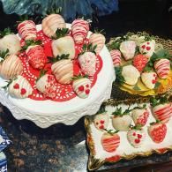 Three decorated strawberry-topped cakes on a dark countertop