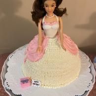 Decorative doll cake with pink and cream frosting on a scalloped white cake board