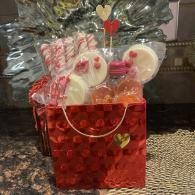 Red gift basket with candy canes, lollipops, and festive packaging on a countertop.