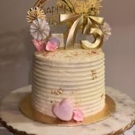 White ribbed cake with gold “75” topper and pastel flowers on a marble stand