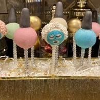 Pastel cake pops on sticks with pink, blue, and turquoise decorations on a gold tray