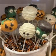 Halloween-themed cake pops in a bucket, decorated like pumpkins, ghosts, and monsters on sticks