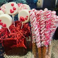 Red and white heart-shaped lollipops and candy sticks arranged in a gift basket and clear containers.