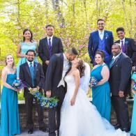 Wedding party posing outdoors in formal attire, with the bride and groom kissing in front of bright yellow trees.