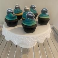 Five teal and black frosted cupcakes on a white lace cake stand.