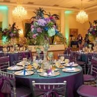 Elegant banquet hall with round tables, purple decor, and tall floral centerpieces