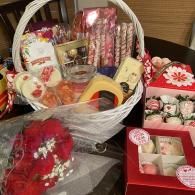 Gift basket of assorted sweets, snacks, and a red floral box on a table.