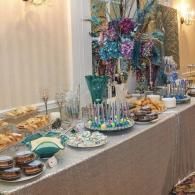 Elegant buffet table with teal and silver decor, glassware, plates, and desserts at an event.