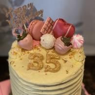Pink and gold birthday cake topped with macarons, meringues, and a glittery “35” topper