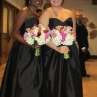 Two women in black strapless gowns holding bouquets at a formal event