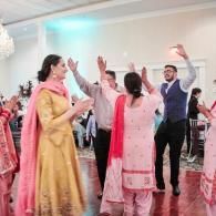 People dancing with raised arms at a festive indoor celebration, wearing colorful traditional outfits
