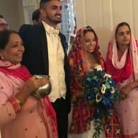 Group of four people standing indoors, smiling, with one holding a bouquet of flowers and another holding a bowl.
