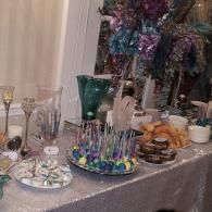 Decorated dessert table with cakes, pastries, colorful drinks, and silver tinsel backdrop