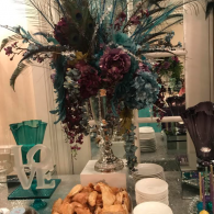 Elegant buffet table with tall floral centerpiece, teal decor, pastries, and stacked plates