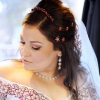 Bride in white veil with floral hairpins and pearl necklace, looking down in a car