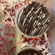 Chocolate-drizzled cupcake on red and white shredded filling, with a partially visible pink-frosted cupcake below